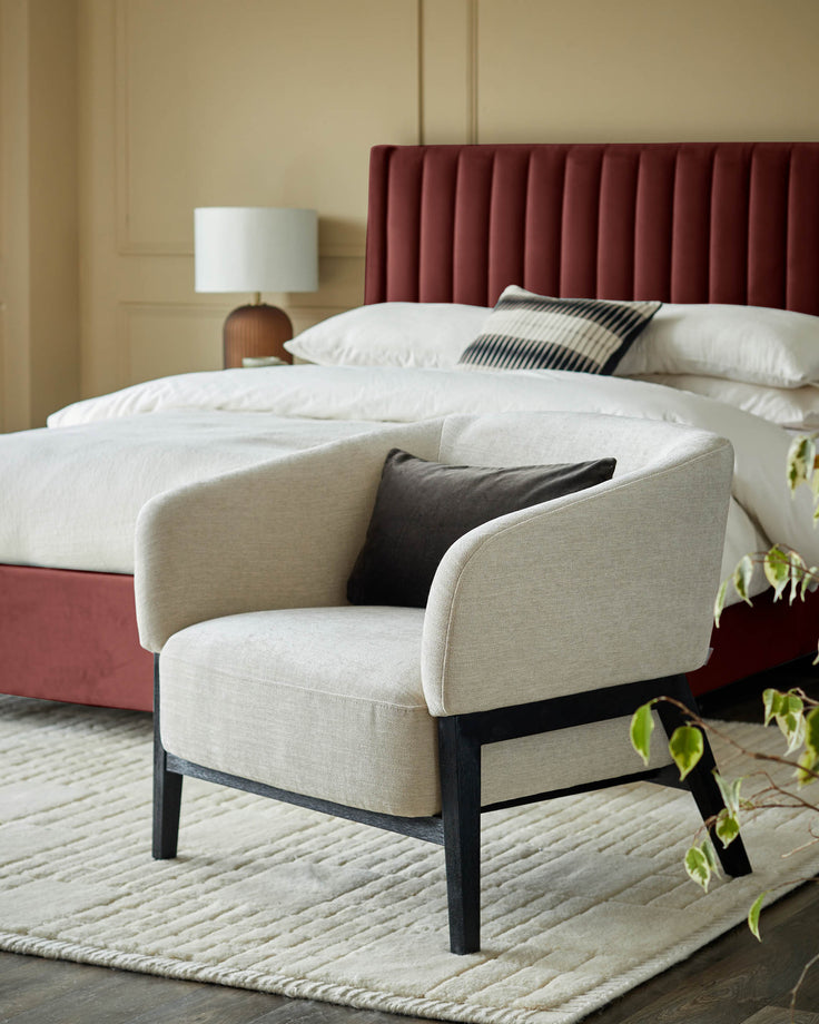 Stylish armchair with a contrasting dark frame, placed next to a bed with a plush headboard and crisp white linens.