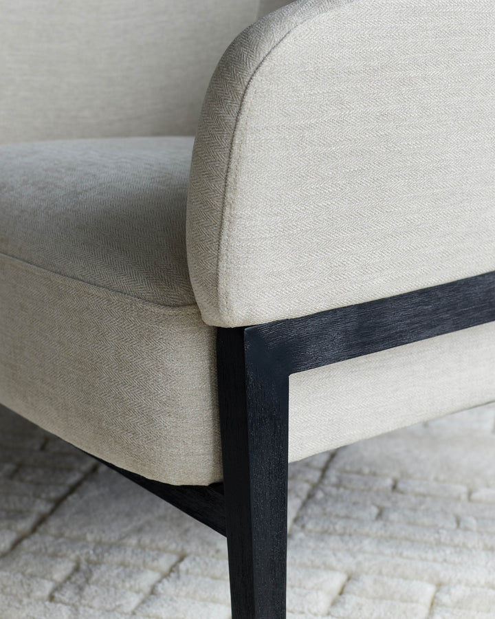 Close-up of an upholstered chair with black wood frame. The neutral fabric is textured.