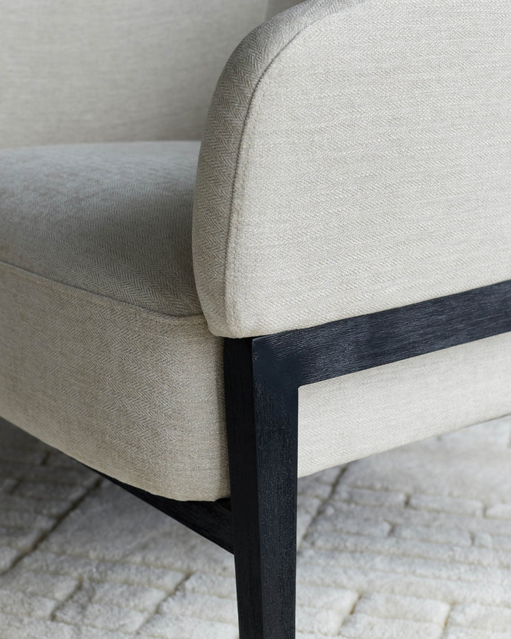 Close-up of an upholstered chair with black wood frame. The neutral fabric is textured.
