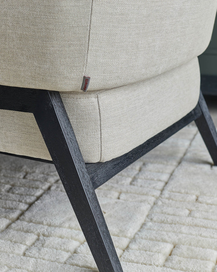 Close-up of an armchair with a light fabric and dark wood frame, showcasing elegant design and quality craftsmanship.