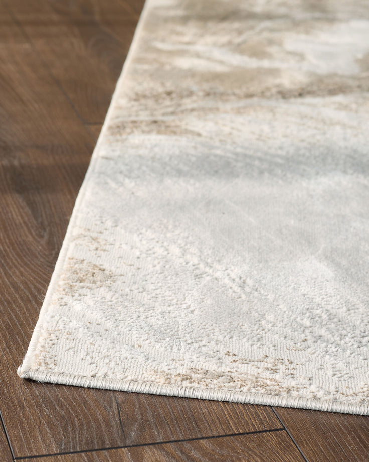 Perla Expression medium textured rug in silver, shown at an angle on dark wood flooring, displaying its woven texture.