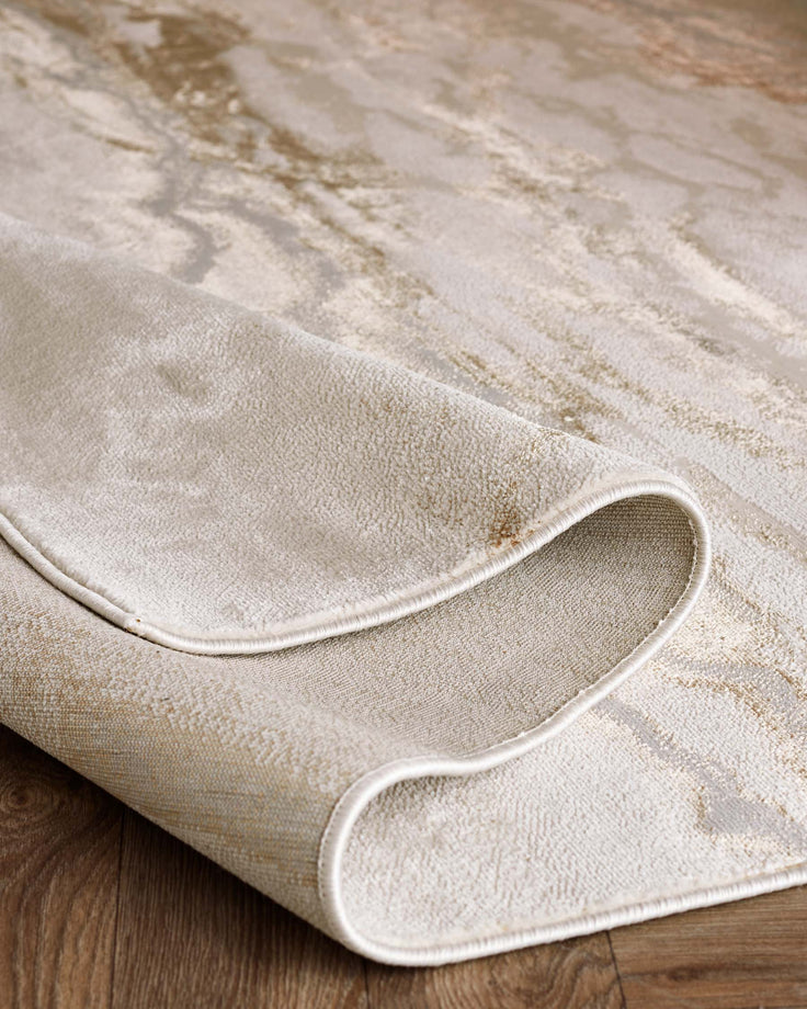 Elegant, textured area rug with a mix of beige and light brown tones, featuring a subtle abstract pattern and neatly finished edges, displayed on a hardwood floor.