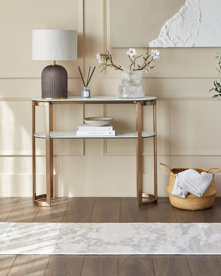 A console table with marble tops and a bronze metal frame. Table lamp, diffuser, vase, books and basket are on display.
