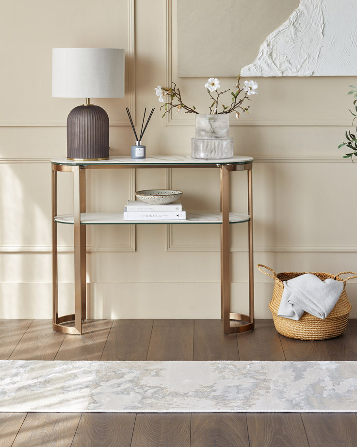 A console table with marble tops and a bronze metal frame. Table lamp, diffuser, vase, books and basket are on display.