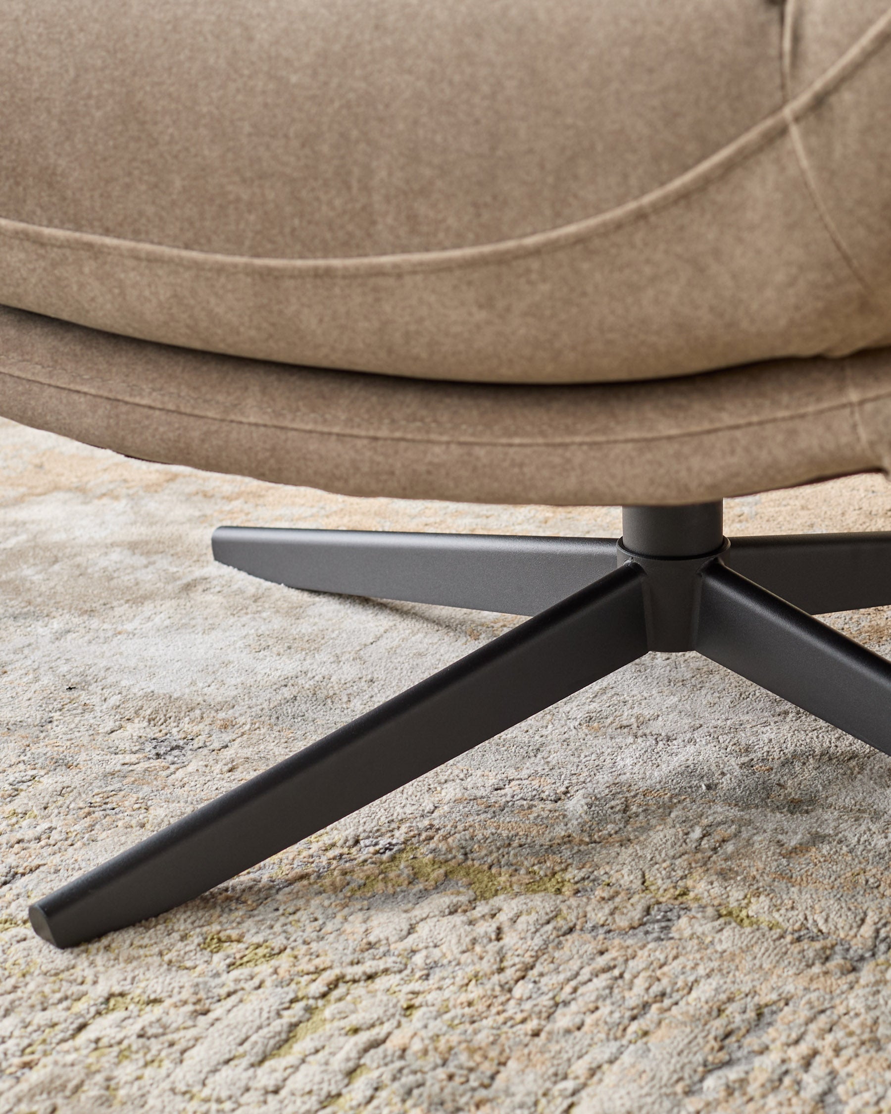 Mocha fabric accent chair with black metal legs, close-up of splayed base on light carpet.