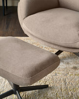 Mocha fabric accent chair and footstool with curved design on black legs, positioned on a cream textured rug.