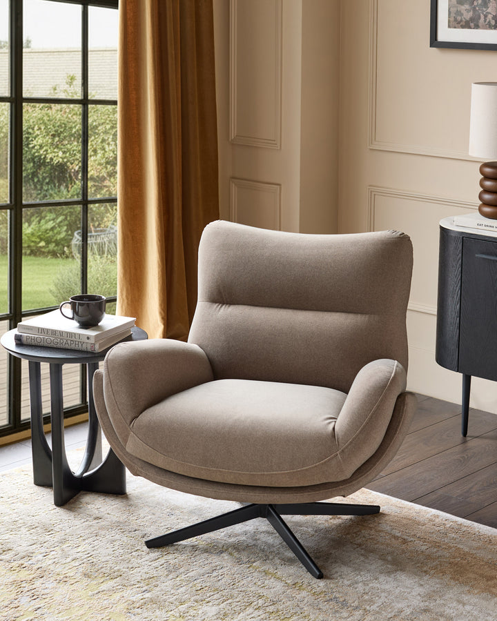 Mocha fabric accent chair with curved back, padded armrests, and black splayed legs in a bright room setting.