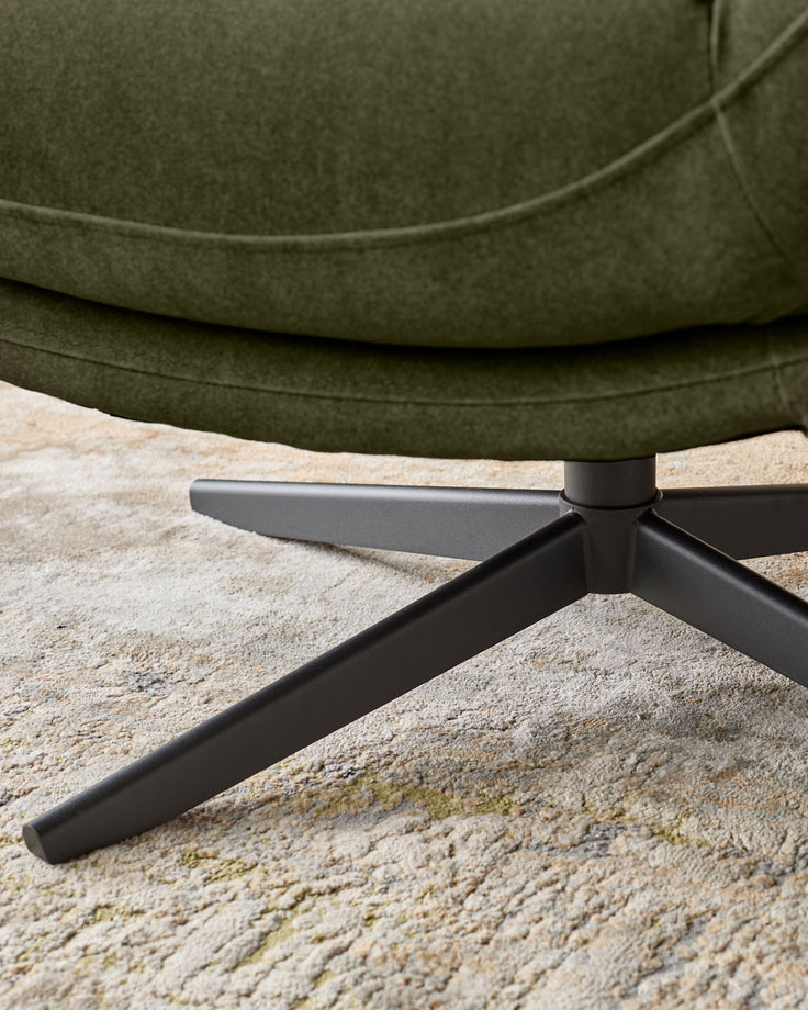 Olive green velvet accent chair with black tripod legs, close-up detail of leg base on concrete surface.