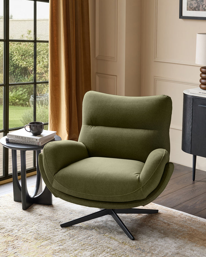 Piper accent chair in olive green velvet with curved back, padded armrests, and black splayed legs in a bright living room.