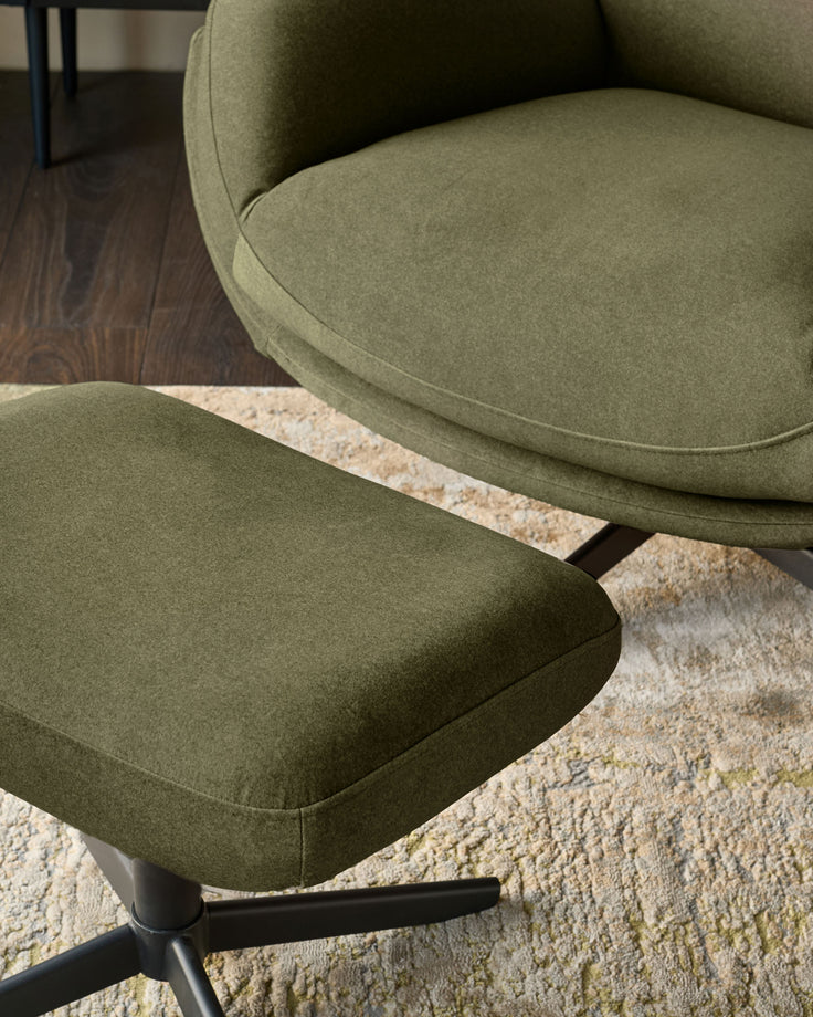 Piper accent chair with footstool in olive green velvet, shown from a side angle on a cream textured rug with dark wood flooring visible.