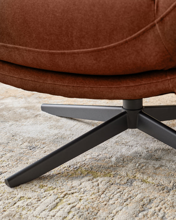Brown fabric accent chair with black metal legs on a beige rug, close-up of base.