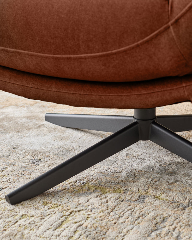 Brown fabric accent chair with black metal legs on a beige rug, close-up of base.