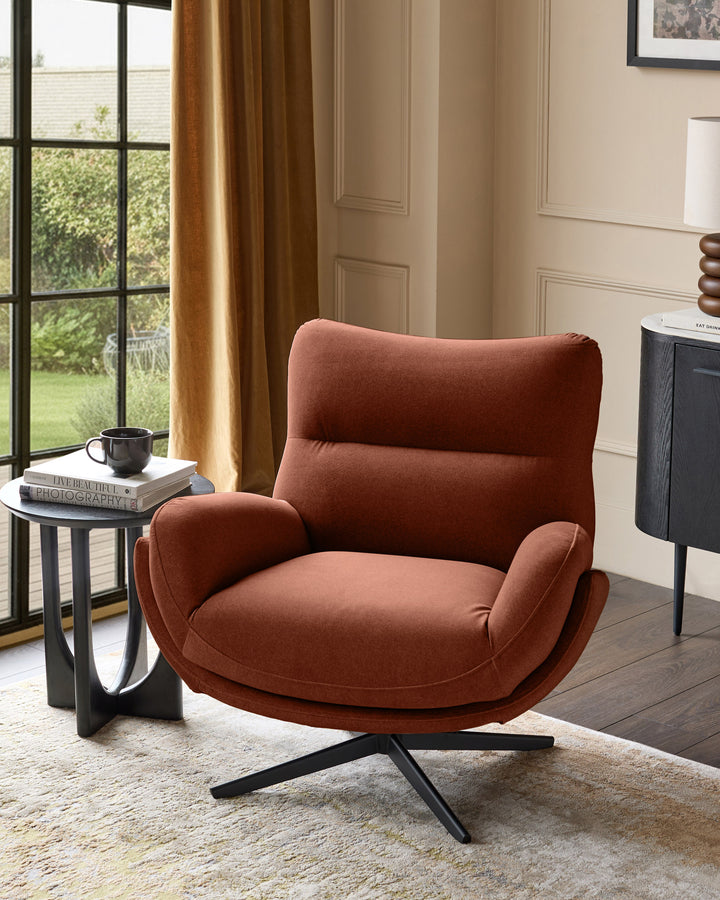 Toffee-red fabric accent chair with curved back, padded armrests, and black splayed legs, positioned in a modern living room.