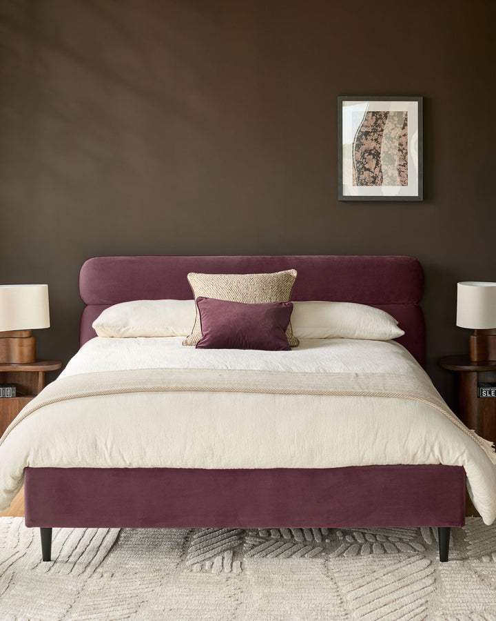Preston king-size bed in plum velvet with curved headboard and footboard, styled with cream bedding and decorative pillows.