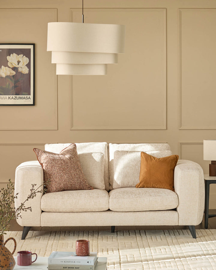 Quinn 2-seater sofa in natural fabric with rounded arms, displayed in a beige living room with decorative pillows.