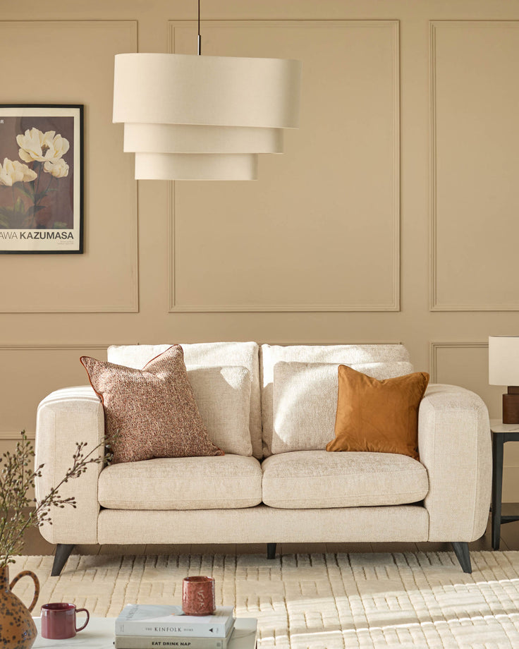 Quinn 2-seater sofa in natural fabric with rounded arms, displayed in a beige living room with decorative pillows.