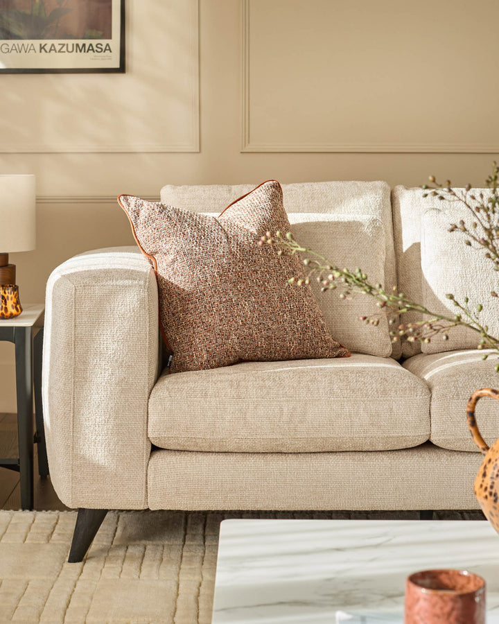 Quinn 2-seater sofa in natural fabric with rounded arms, tapered legs, and decorative pillows in a styled living room setting.