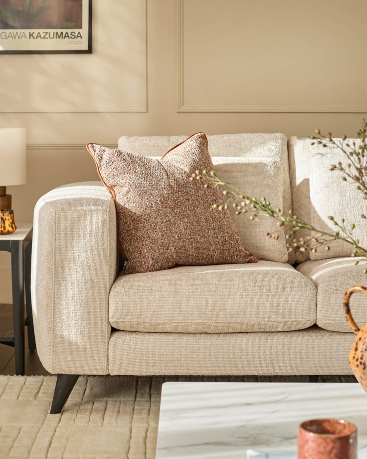 Quinn 2-seater sofa in natural fabric with rounded arms, tapered legs, and decorative pillows in a styled living room setting.