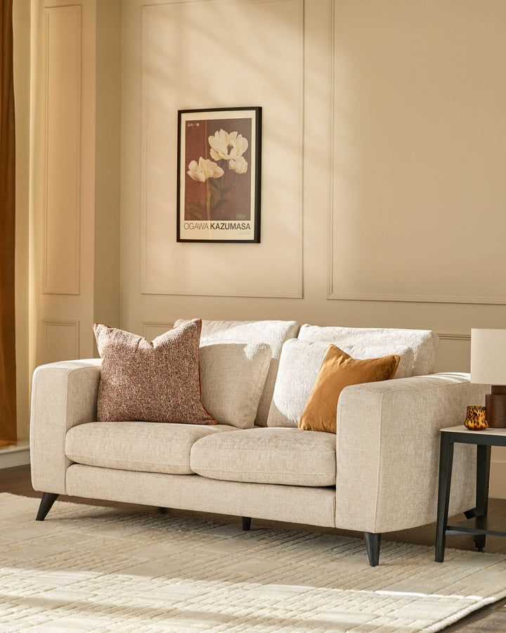 Quinn 2-seater sofa in natural fabric with dark wooden legs, styled with decorative pillows in a neutral living room setting.