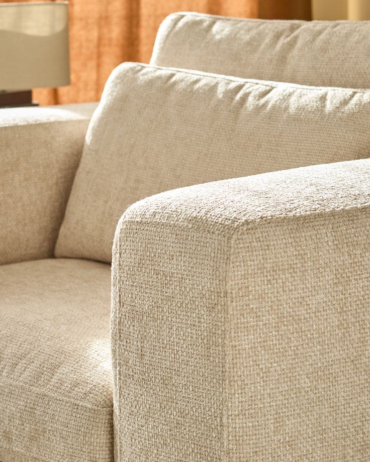 Quinn armchair in natural fabric, close-up of upholstered arm and cushioned seat detail.