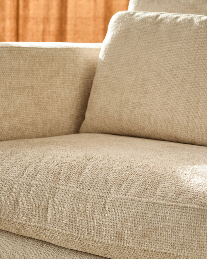 Quinn armchair in natural fabric, close-up of seat and cushioned armrests with white piping detail.