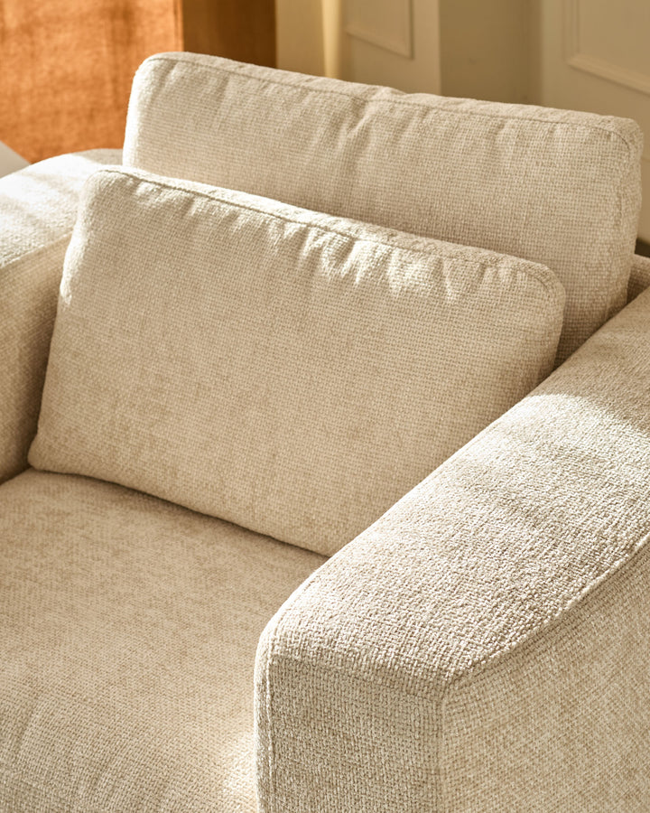 Quinn Armchair in natural fabric, close-up detail showing beige upholstery, cushioned back and armrests with textured weave.