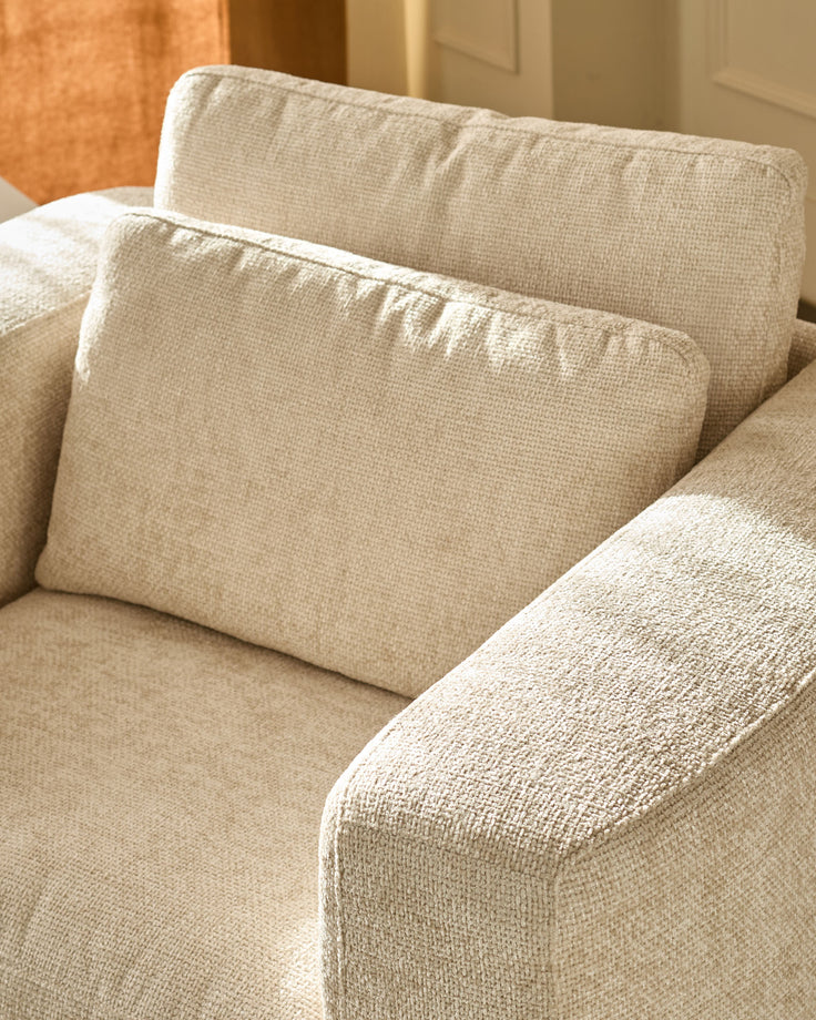 Quinn Armchair in natural fabric, close-up detail showing beige upholstery, cushioned back and armrests with textured weave.
