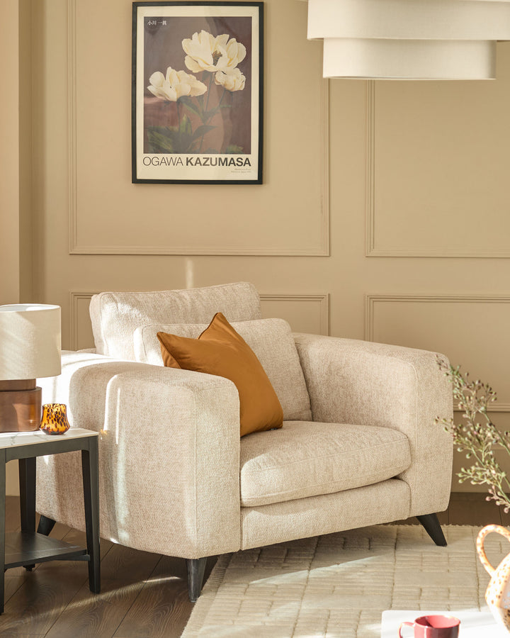 Quinn armchair in natural fabric, featuring curved arms and angled legs, styled in a beige living room setting.