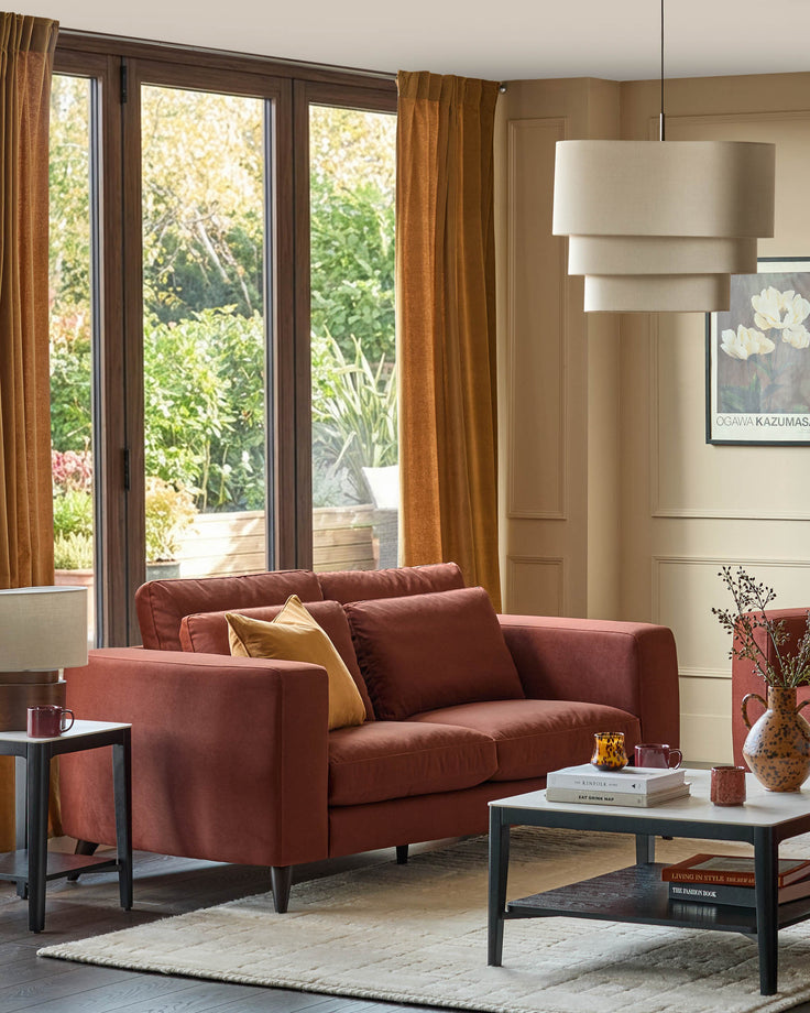 Quinn 2-seater sofa in toffee red fabric, displayed in a modern living room with gold cushion and dark legs.