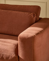 Quinn armchair in toffee-red fabric, close-up detail showing rolled arm and seat cushioning against cream wall.