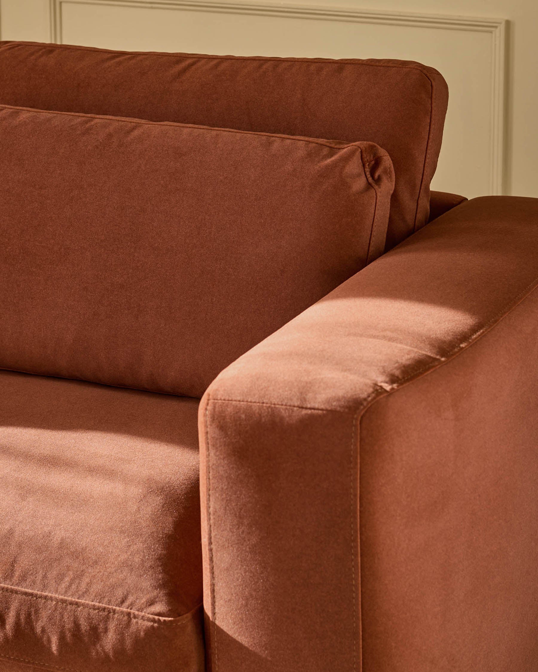 Quinn armchair in toffee-red fabric, close-up detail showing rolled arm and seat cushioning against cream wall.