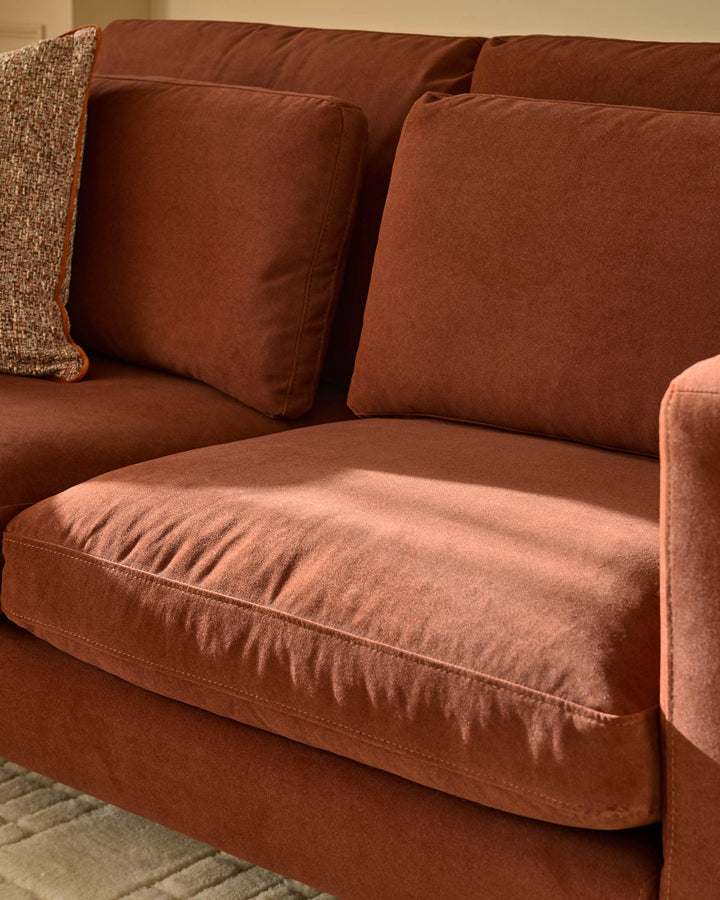 Quinn 2-seater sofa in toffee-red fabric, showing seat cushion detail and decorative pillows from a side angle.