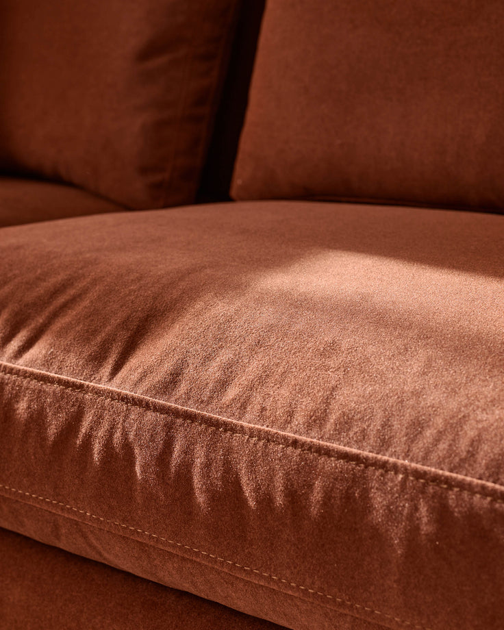 Close-up of toffee-red fabric sofa cushion showing soft texture and stitched seams detail.