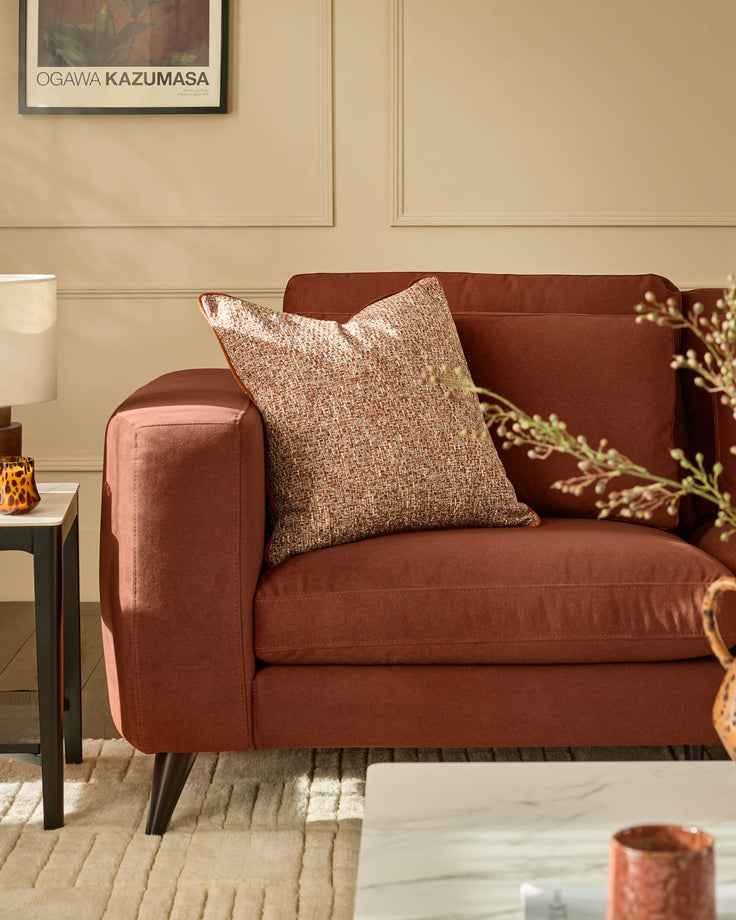 Quinn 2-seater sofa in toffee red fabric with rounded arms, paired with a textured accent pillow in a styled living room.