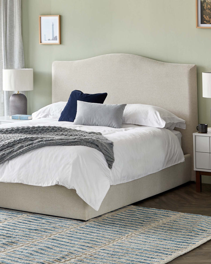 A stylish bedroom featuring a linen upholstered bed, bedside tables, lamps, and a patterned rug, creating a cosy and inviting space.