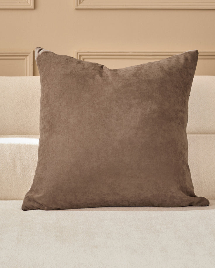 Rania large cushion in taupe, displayed on a cream sofa against a beige paneled wall.