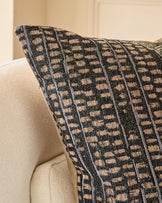 Rania cushion in black with beige checkered pattern, displayed on a cream armchair at an angle.