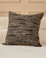 Rania large black cushion with geometric striped pattern in cream and dark green, displayed on a cream sofa against a beige wall.