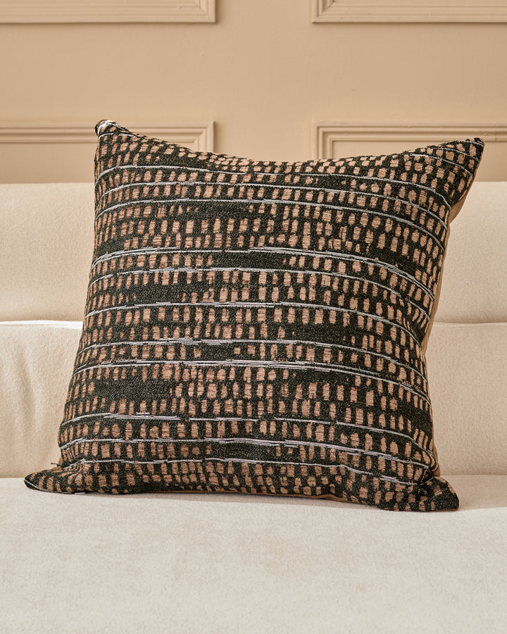Rania large black cushion with geometric striped pattern in cream and dark green, displayed on a cream sofa against a beige wall.