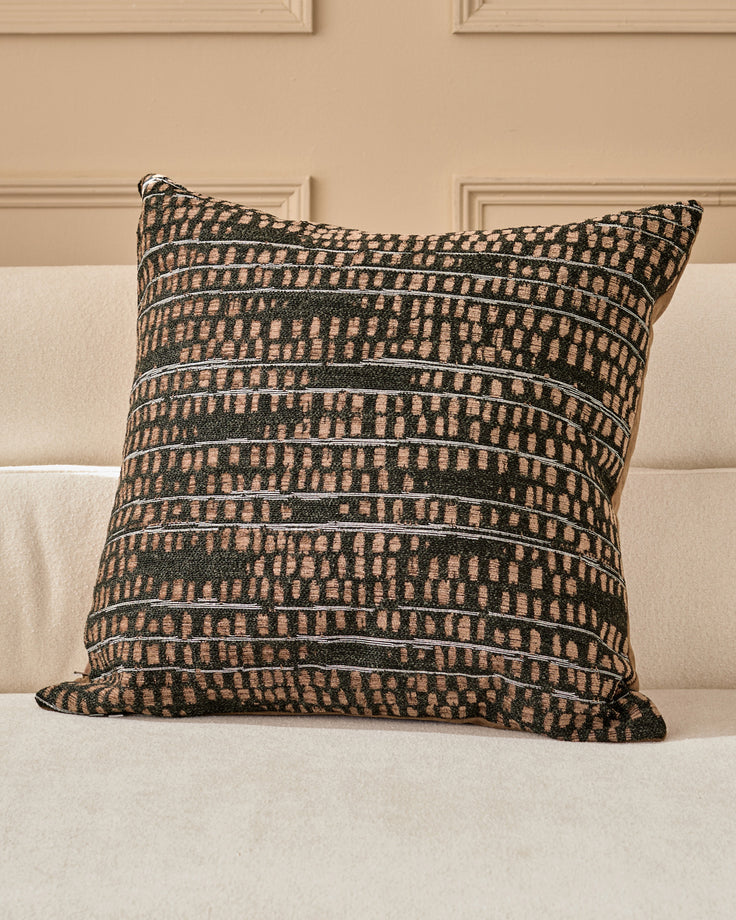 Rania large black cushion with geometric striped pattern in cream and dark green, displayed on a cream sofa against a beige wall.