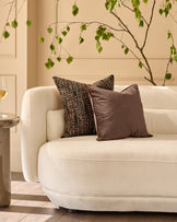 Large black patterned cushion with geometric tribal design, displayed on a cream curved sofa in a minimalist living room setting.