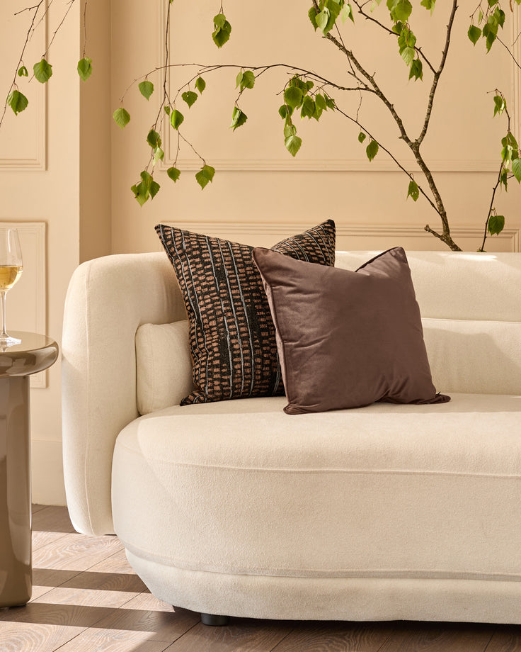 Large black patterned cushion with geometric tribal design, displayed on a cream curved sofa in a minimalist living room setting.