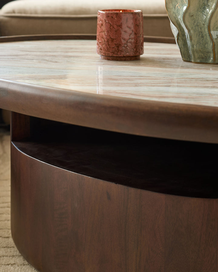 Rayna dark wood coffee table with light marble top, rounded base, styled with candle and vase.