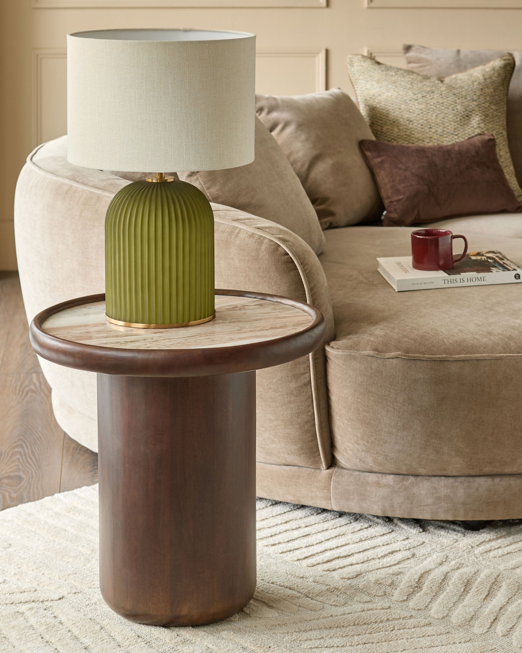 Dark wood cylindrical side table with round light wood top, styled in a modern living room setting with a green ribbed table lamp.