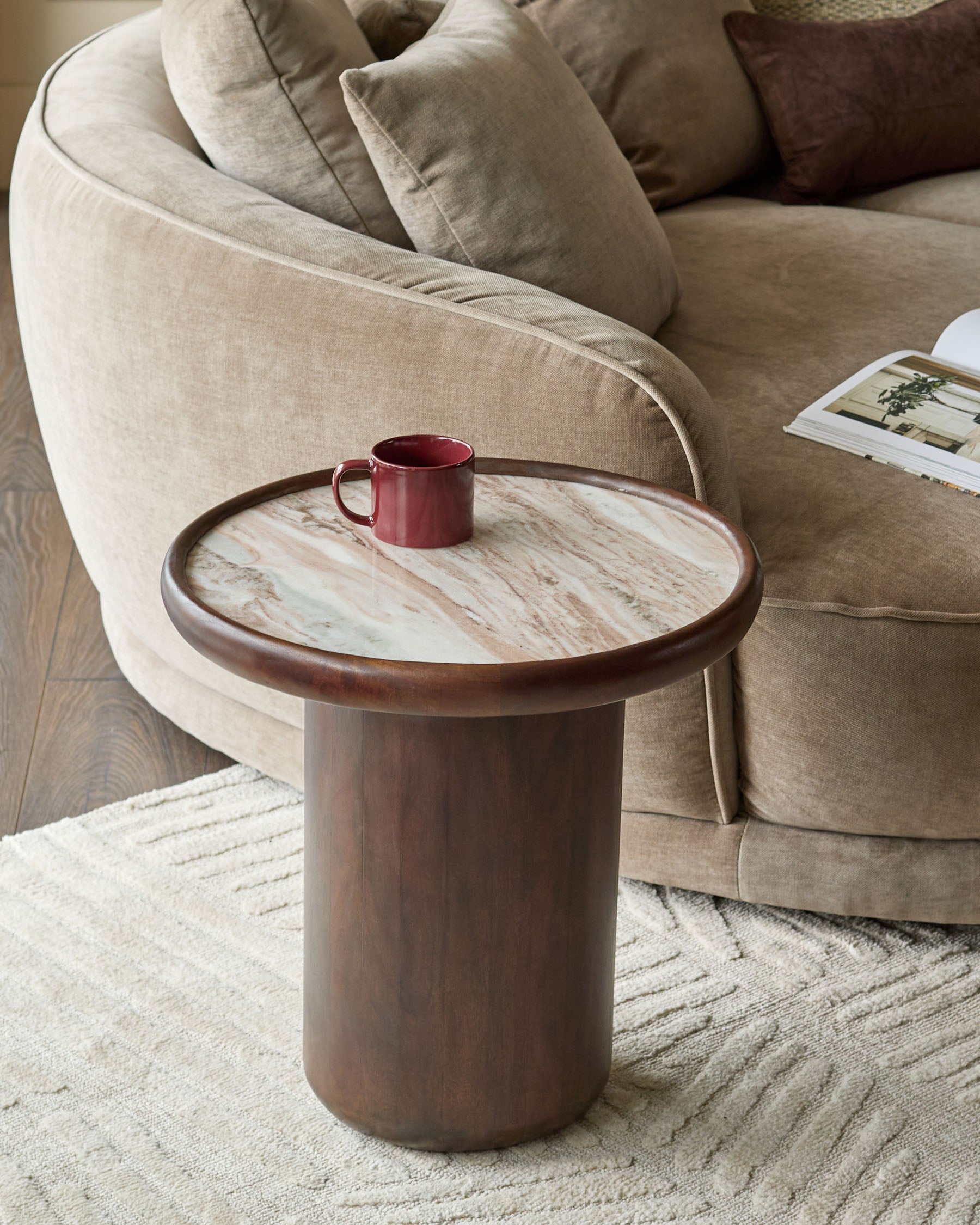 Rayna side table in dark wood with round Toronto marble top, cylindrical pedestal base, styled with burgundy mug in living room setting.
