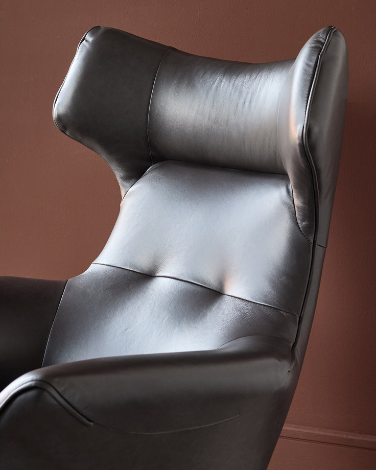 Black leather occasional chair with high back, neck pillow support, and curved wingback design, shown from side angle.