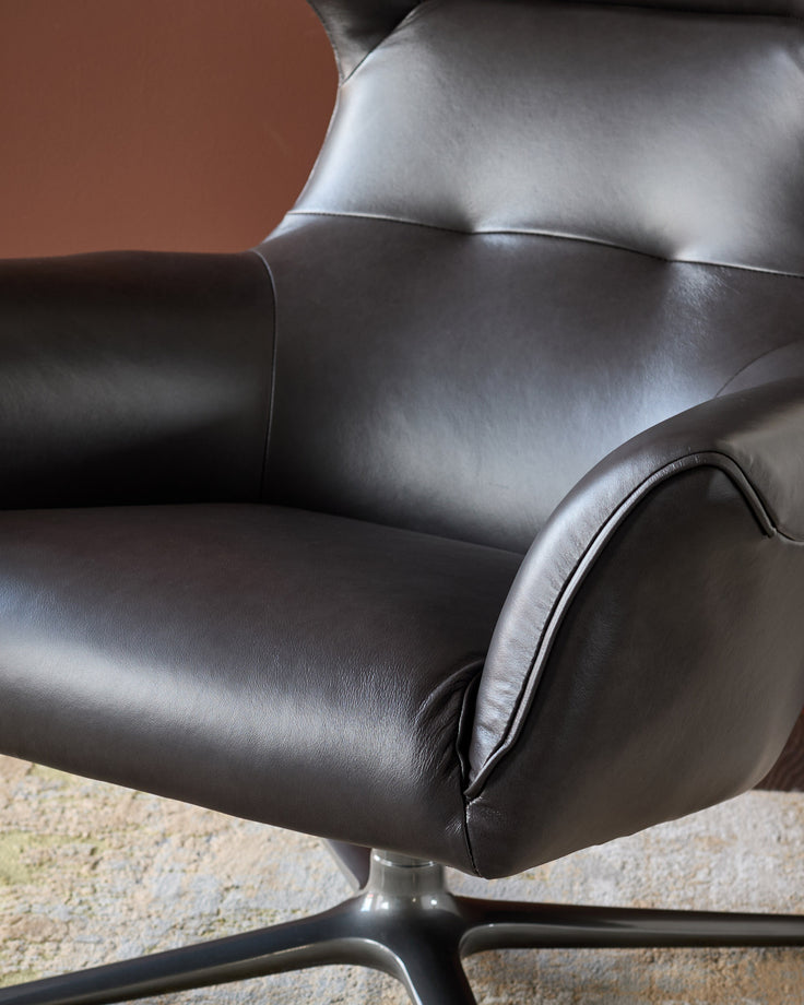 Black leather occasional chair with curved armrests and metal base, shown from side angle.