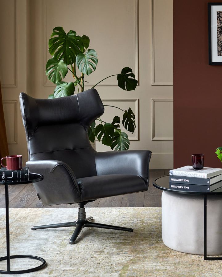 Black leather occasional chair with high back, padded armrests, and swivel base, styled in modern interior setting.