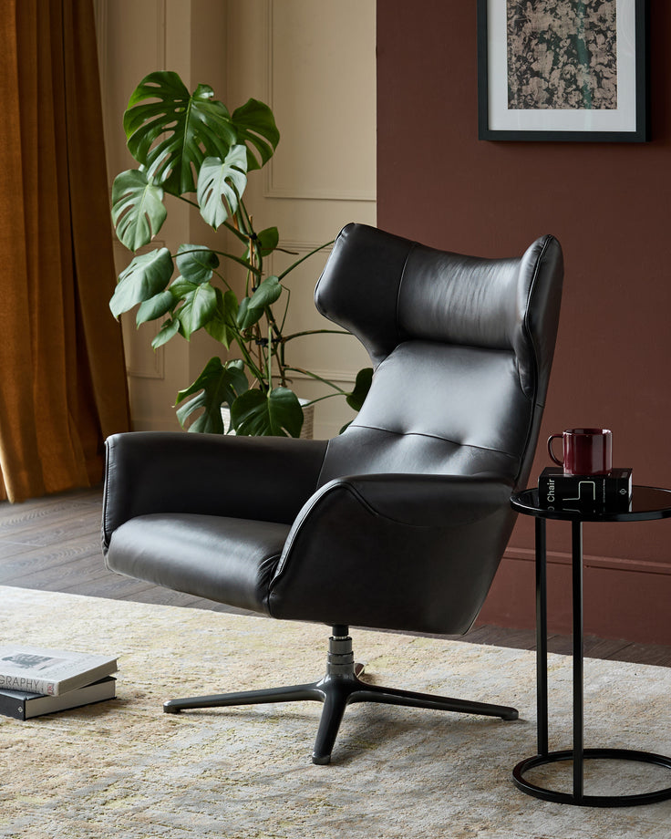 Black leather occasional chair with high back, padded armrests, and swivel base, styled in modern living room setting.