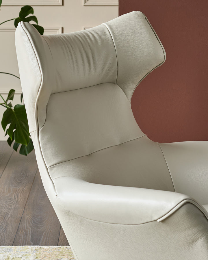 Reign Occasional Chair in natural grey leather, shown at a side angle highlighting its curved high back and cushioned seat.